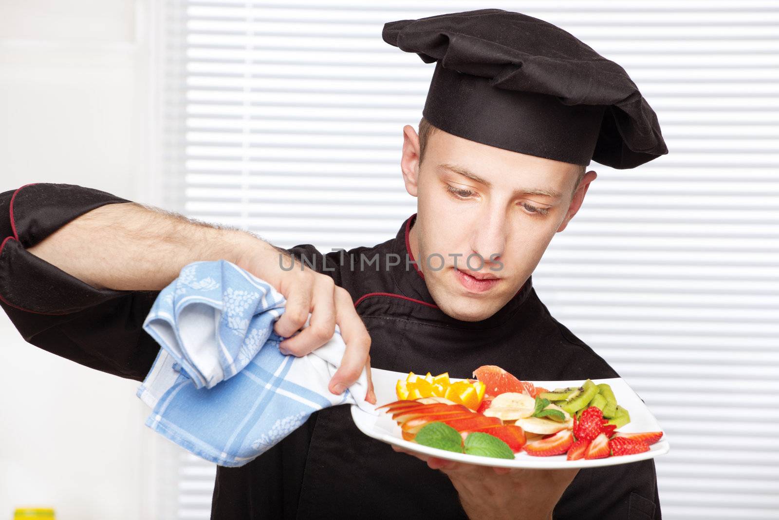 Chef in black uniform cleaning edge of a fruit plate with cloth