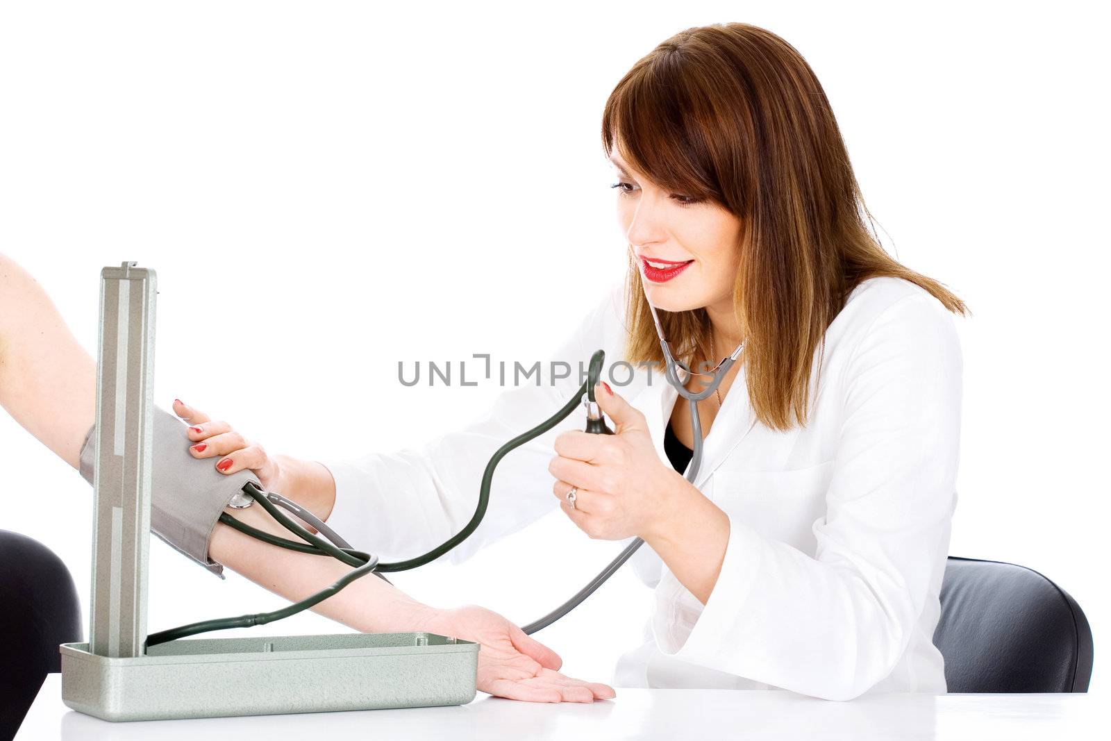 Female nurse measuring patient's blood pressure, with right hand pressing stethoscope and looking at the instrument, isolated on white