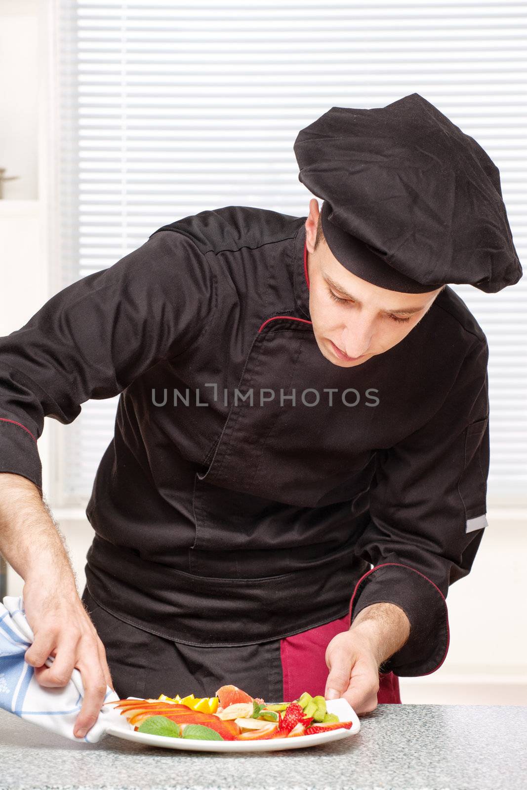 Chef in black uniform cleaning edge of a fruit plate with cloth