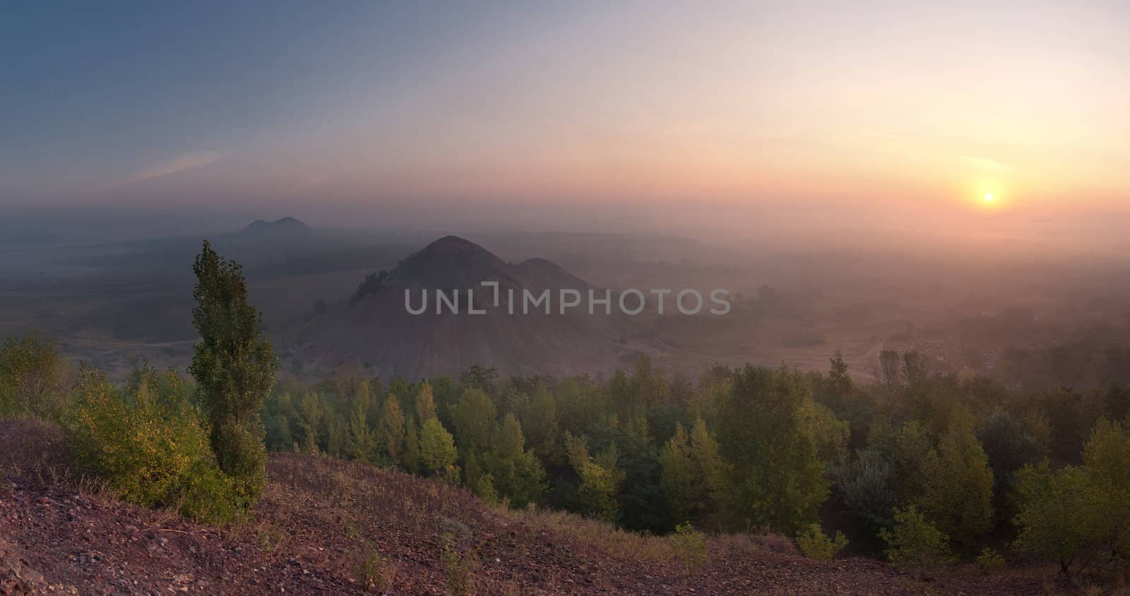 The top view landscape on valley with waste heaps in fog and rising sun