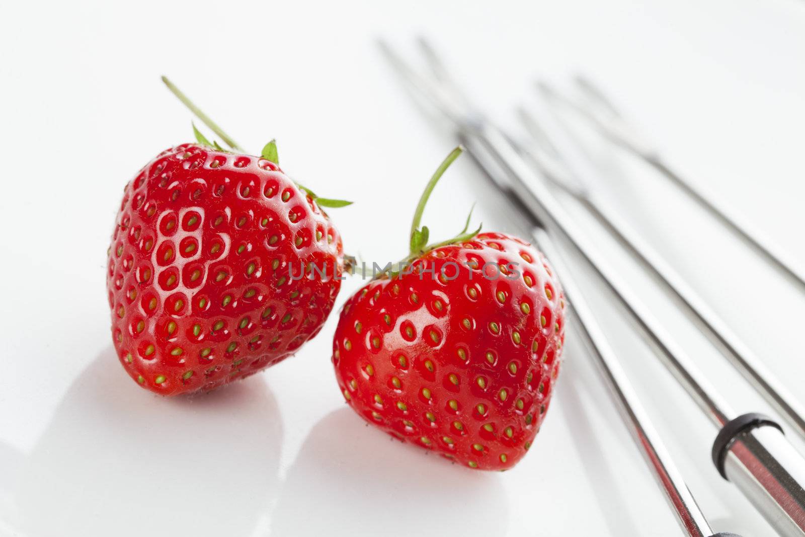 Two freshly picked strawberries on white plate with fondue forks.