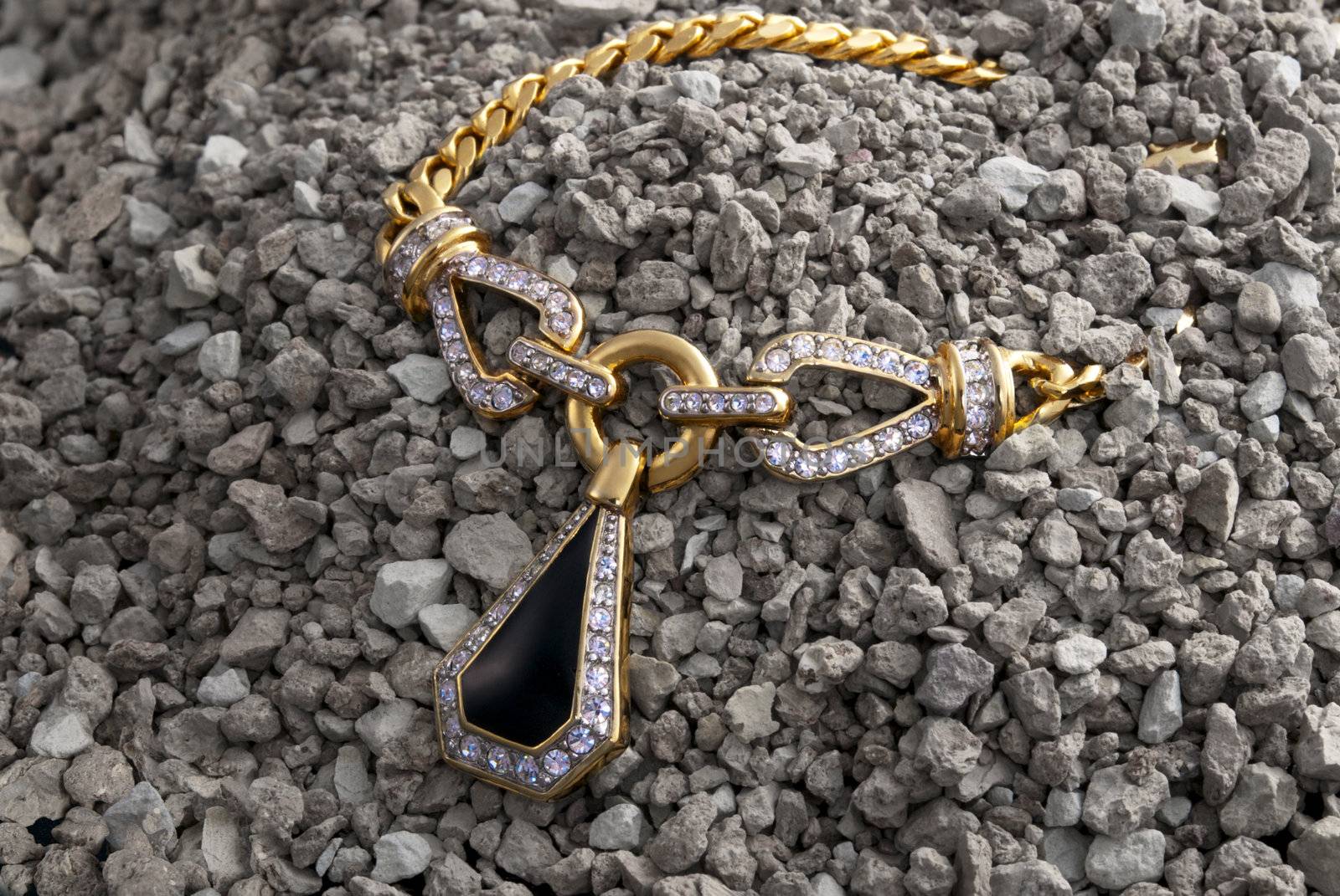 Gold necklace with pendent and diamonds in the pile of pebbles