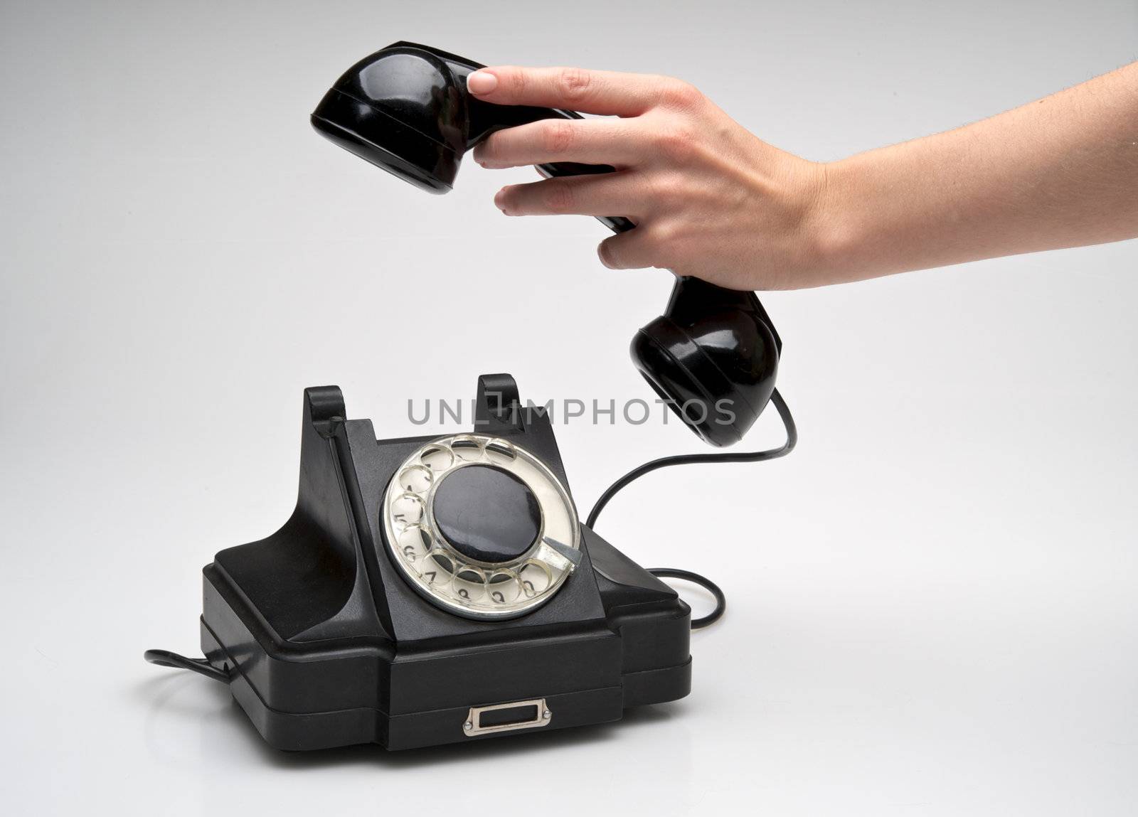 woman hand hanging up the handset of an old black telephone isolated ocer white background