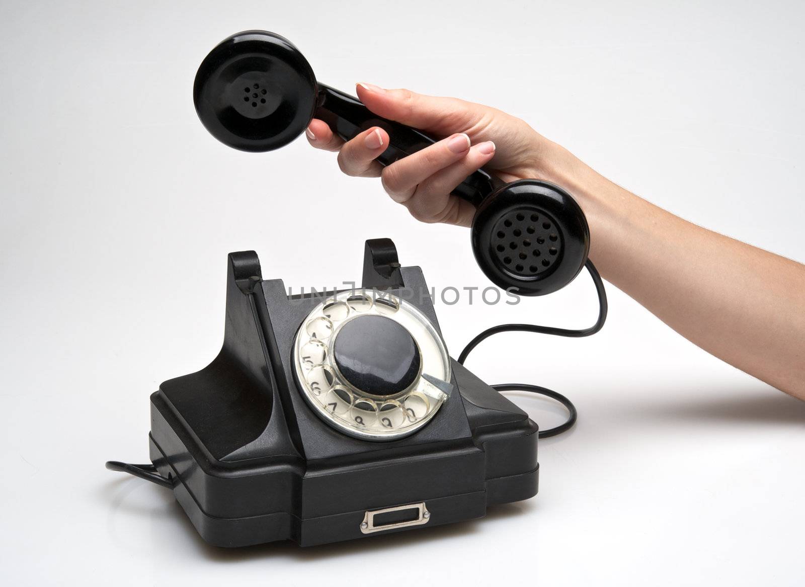 woman hand hanging up the handset of an old black telephone isolated ocer white background