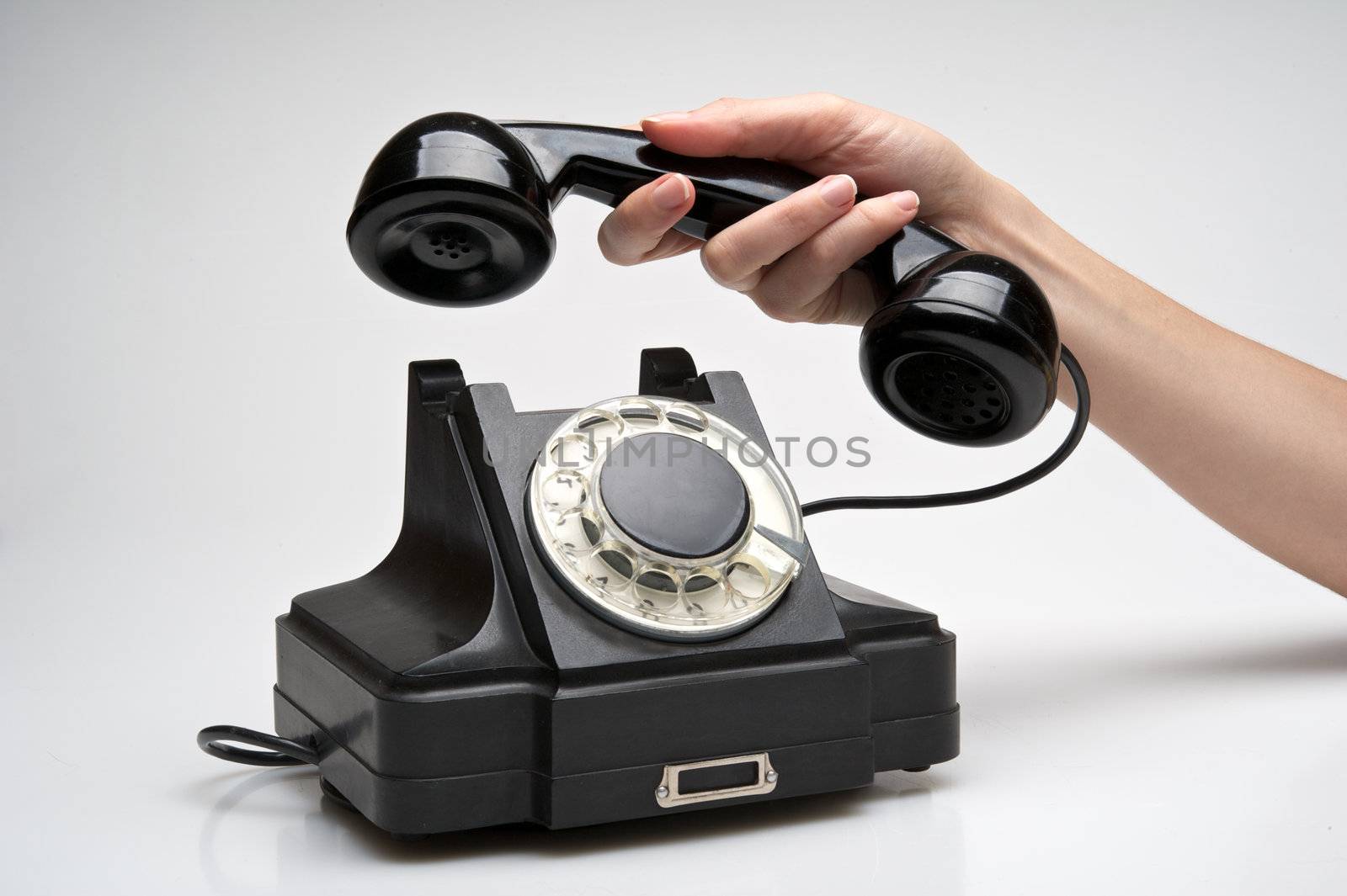 woman hand hanging up the handset of an old black telephone isolated ocer white background