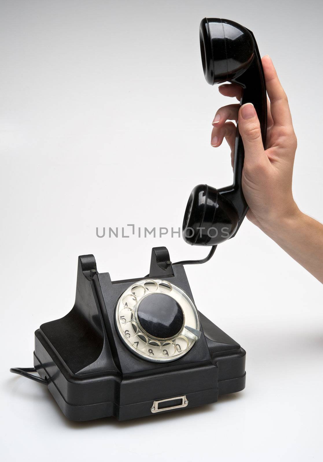 woman hand hanging up the handset of an old black telephone isolated ocer white background