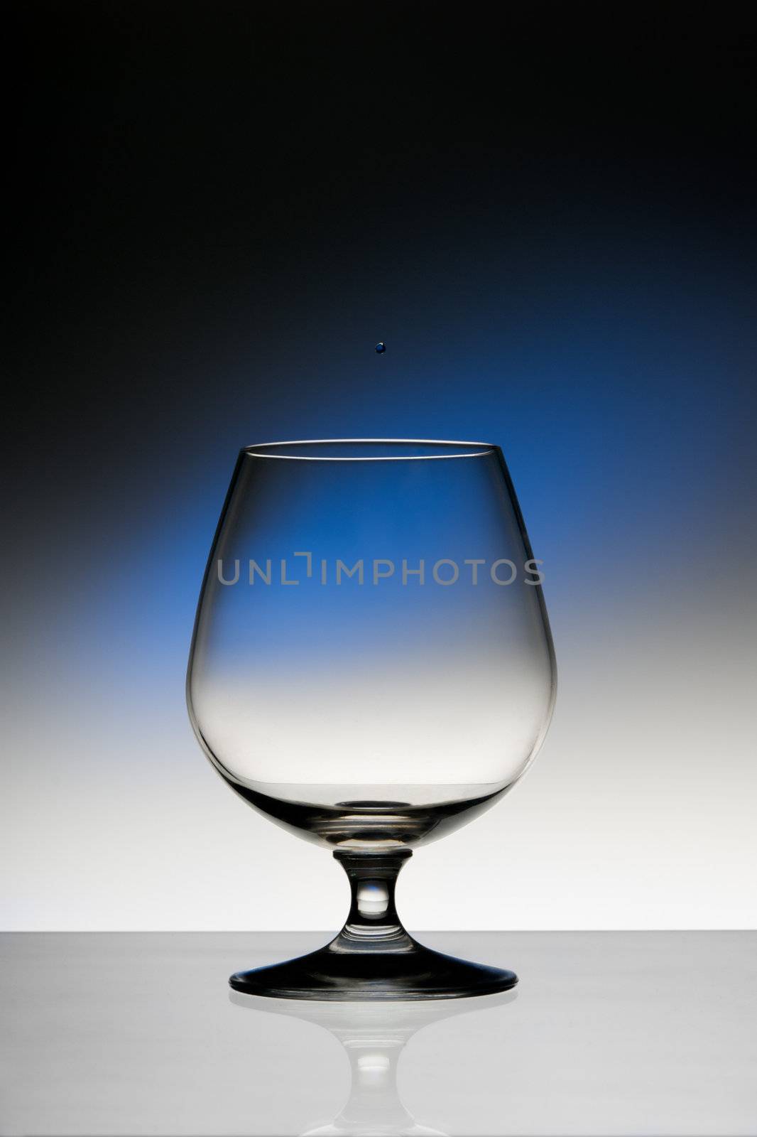 Empty cognac wineglass on dark background with blue spot