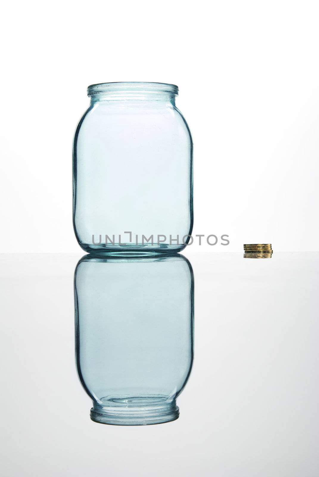 Coins and empty glass jar on white background