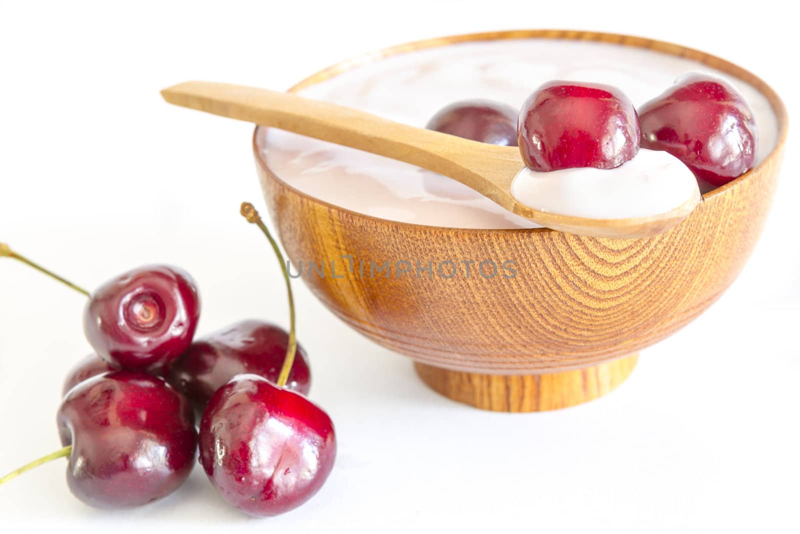 fresh cherries fruits with yogurt in a wooden bowl and spoon