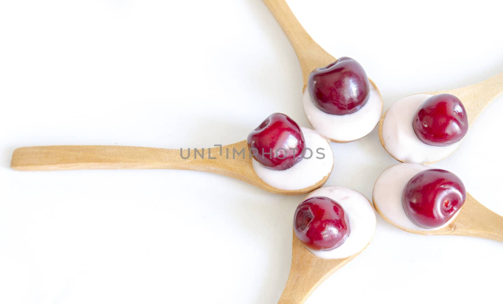 Wooden spoon is with yogurt and fresh cherries on white background