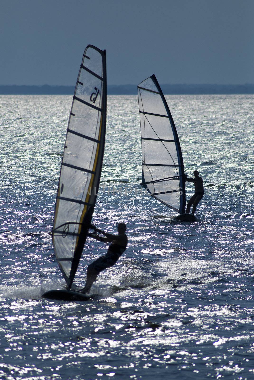 Two windsurfers in patches of light of a sunlight