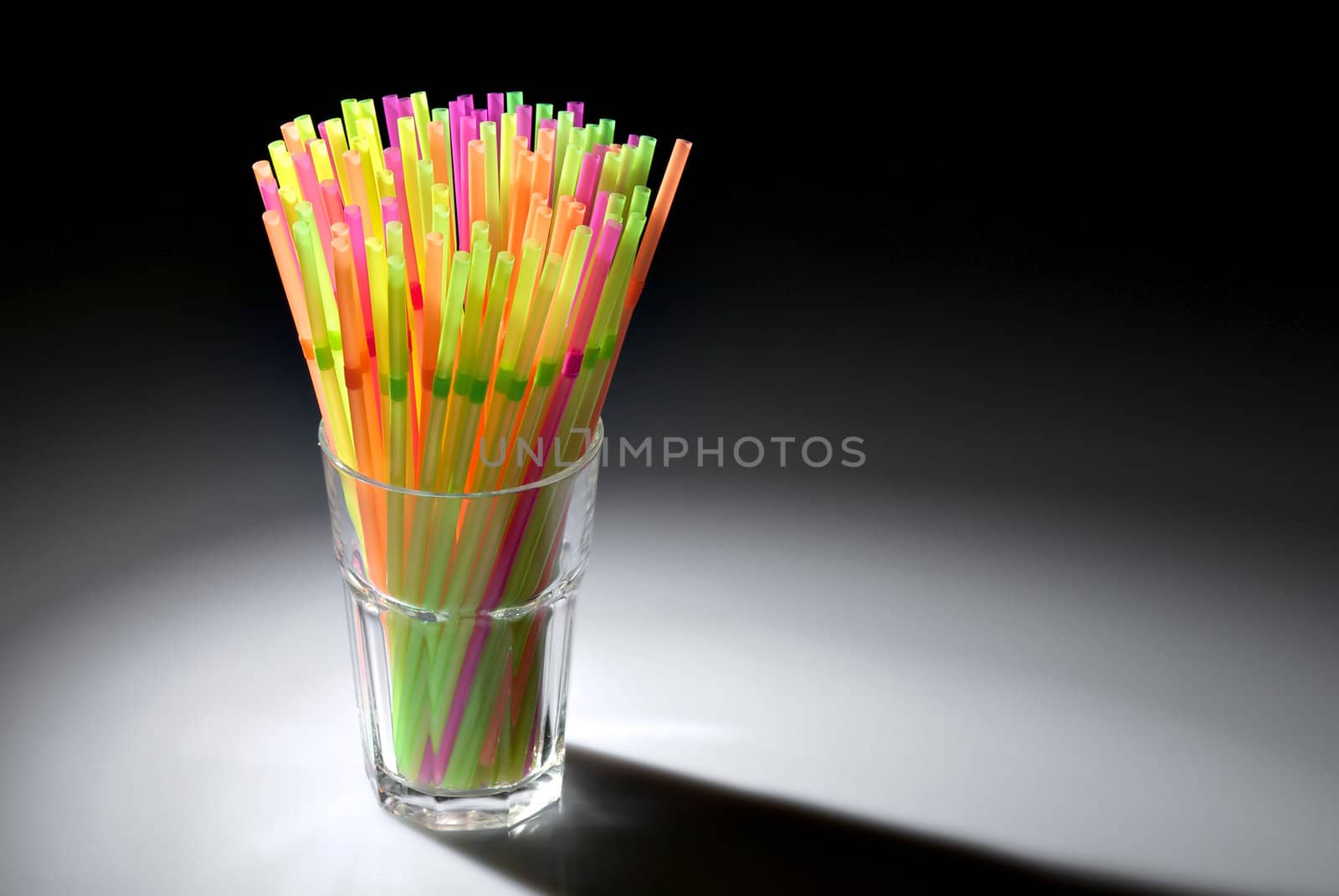 Multicolor flexible straws in the glass in spot of light isolated on black background