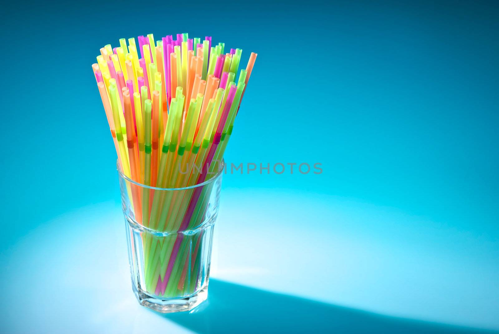 Multicolor flexible straws in the glass in spot of light isolated on blue background