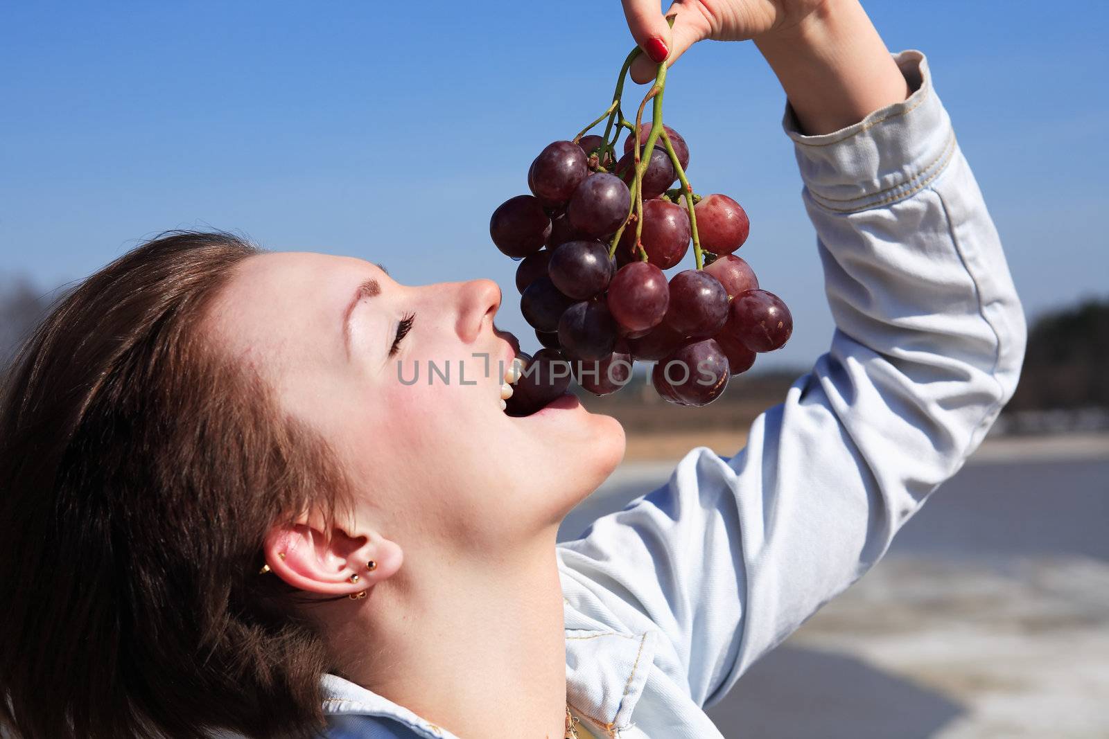 Beautiful young girl eating red grapes outdoor on blue sky background