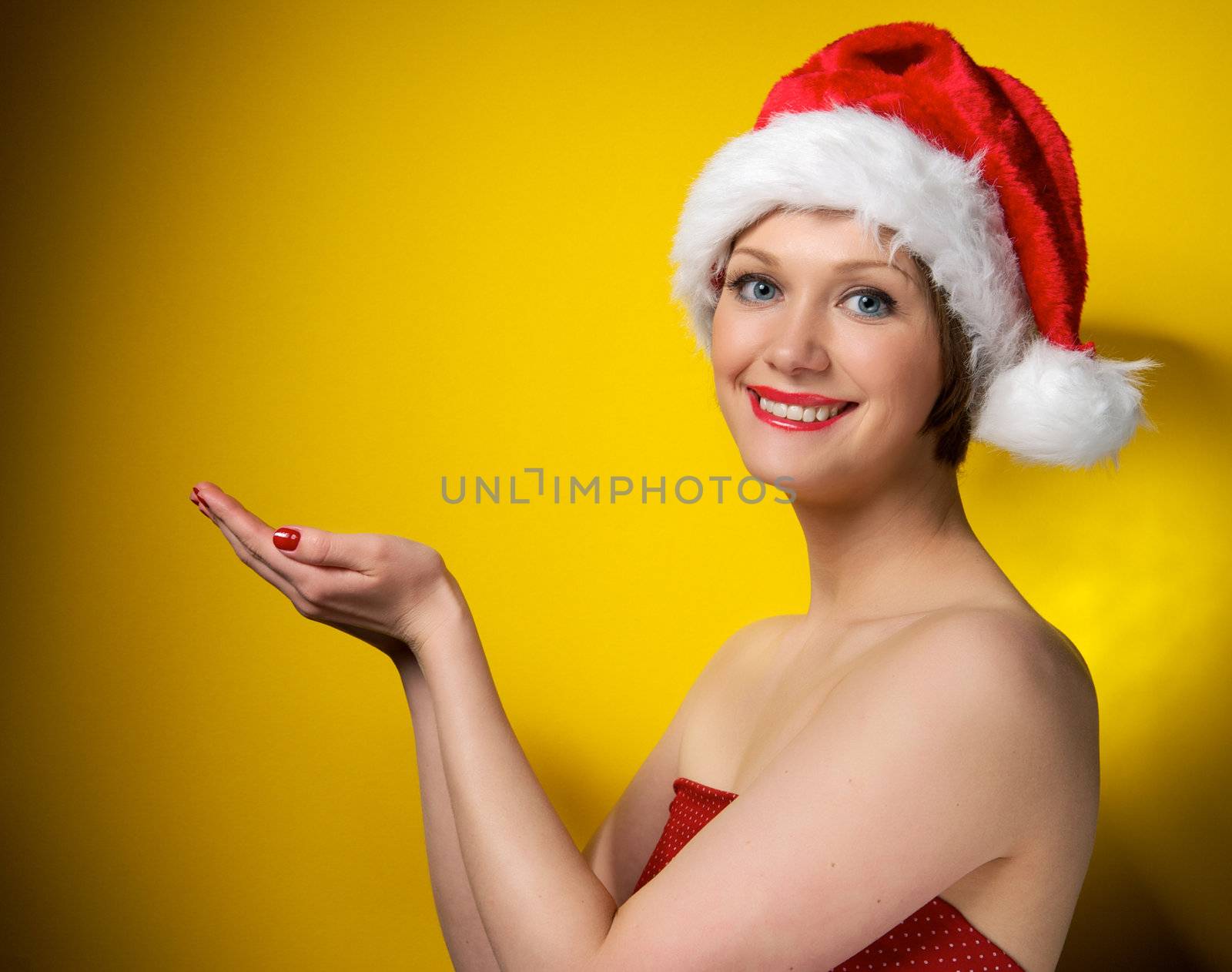 Pretty christmas girl wearing red dress and santa hat, smiling. Isolated on yellow background