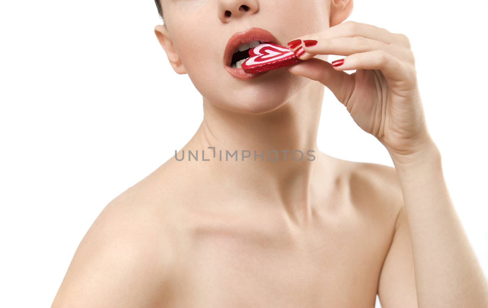 Topless young woman eating heart shaped candy. Face closeup. Isolated on white background