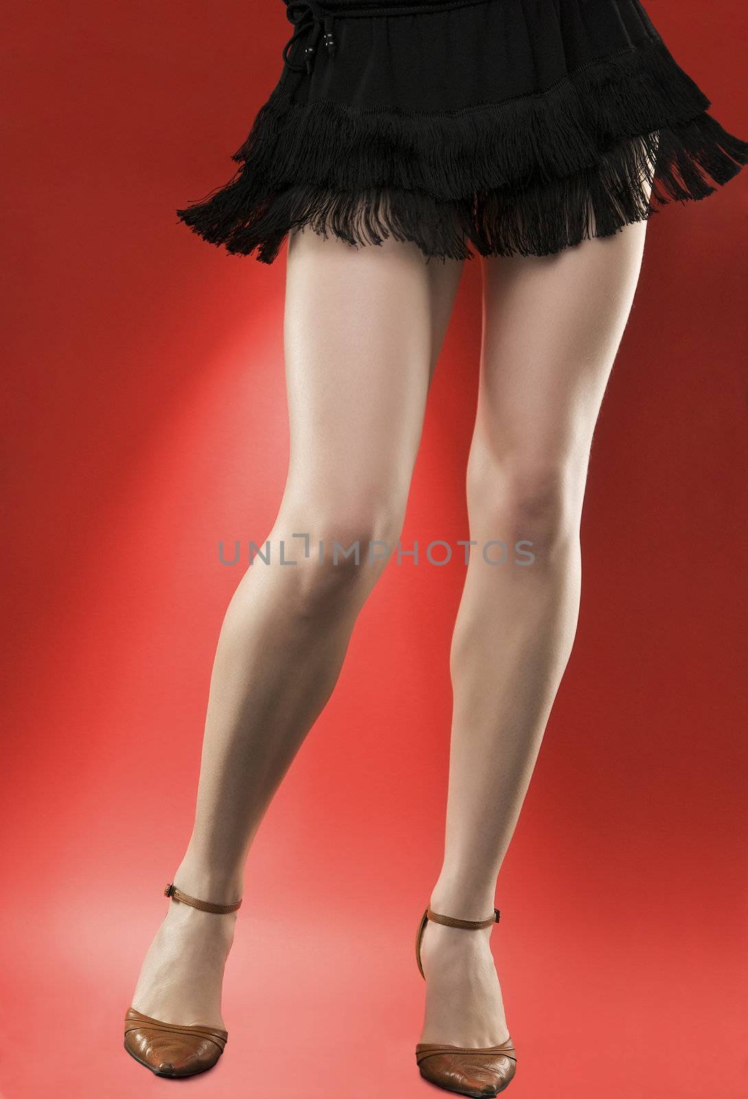 Woman's long legs on high heels dancing over red background