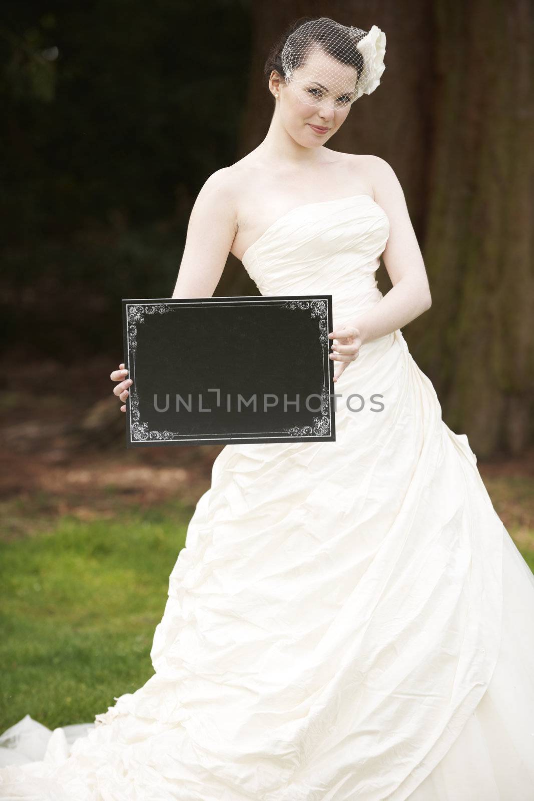 Pretty bride in wedding dress holding a blank board in front of face with space for copy