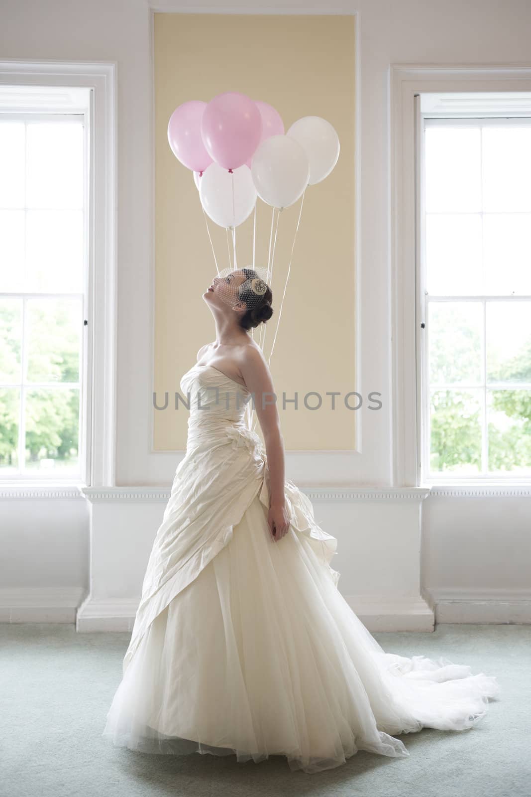 pretty bride in her wedding dress holding ballons in front of windows