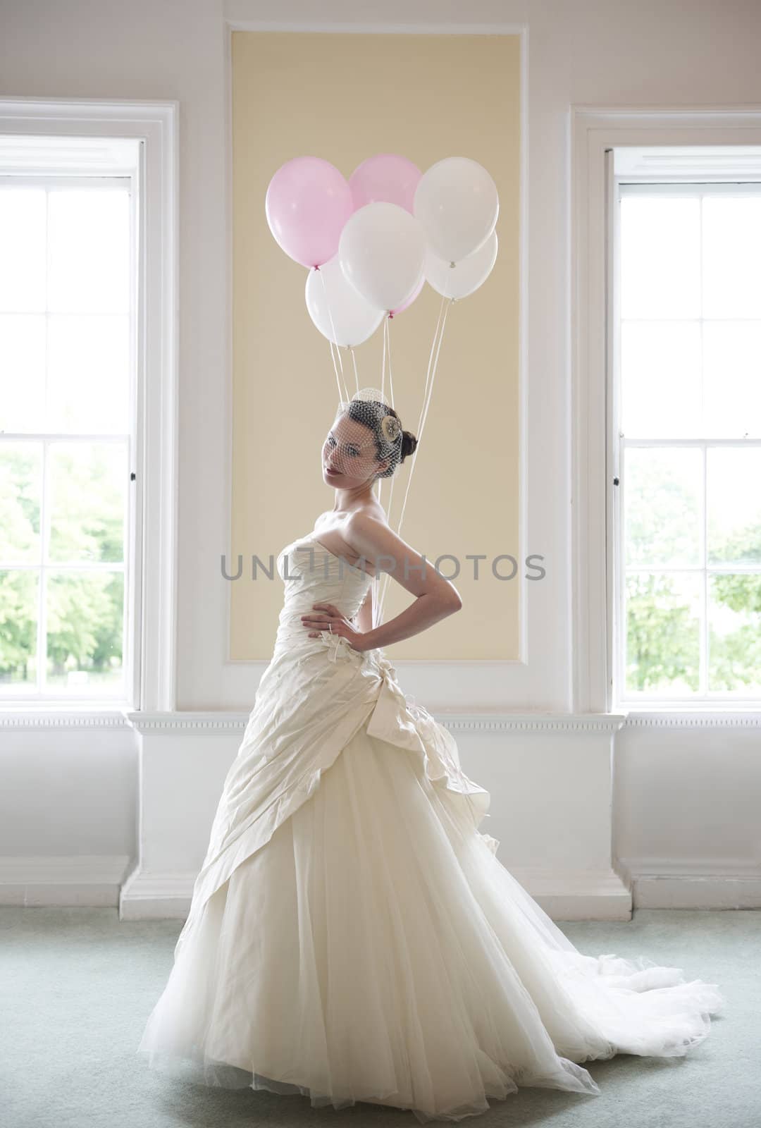 pretty bride in her wedding dress holding ballons in front of windows