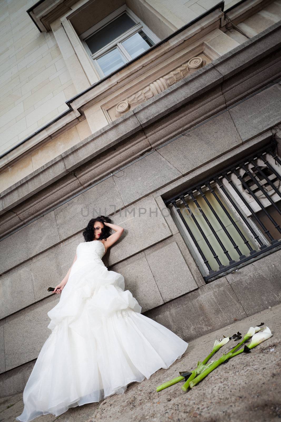 Unhappy bride with wedding dress leaning on a wall, holding broken bottle in one hand
