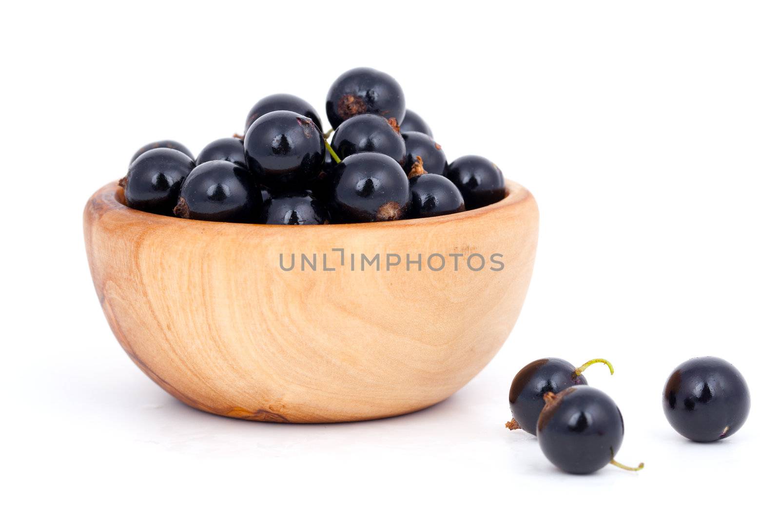 fresh black currants in a wooden bowl, over a white background.