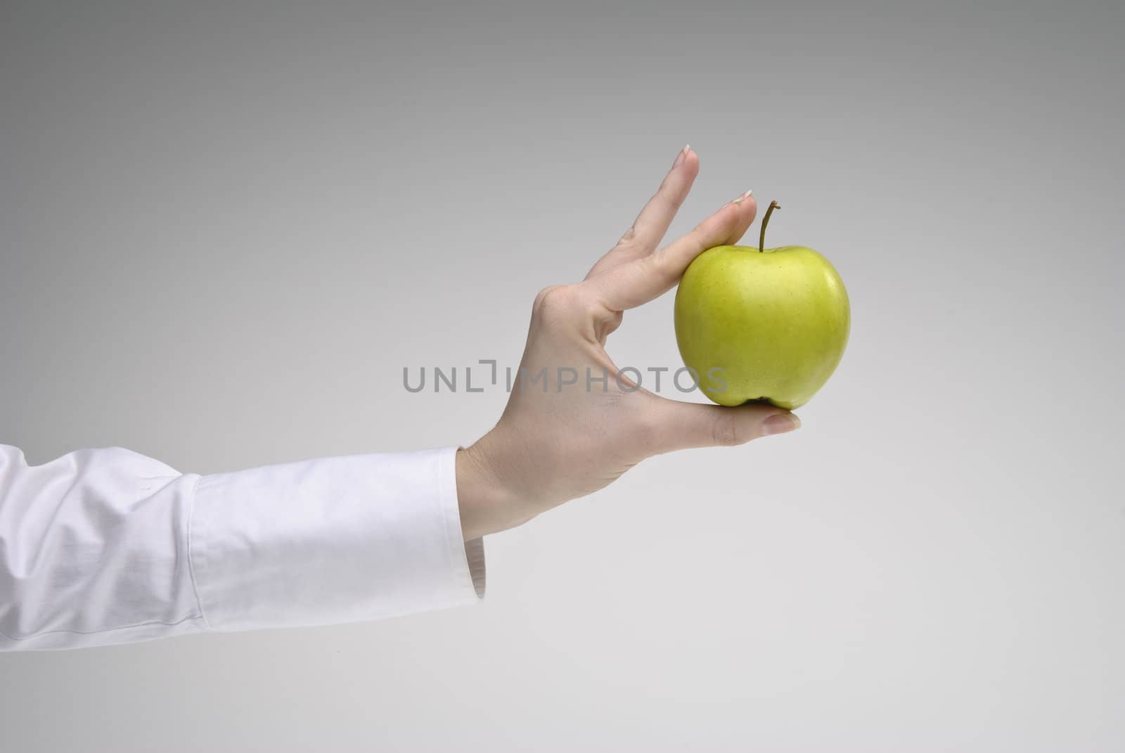 Woman's hand holding green apple over light background