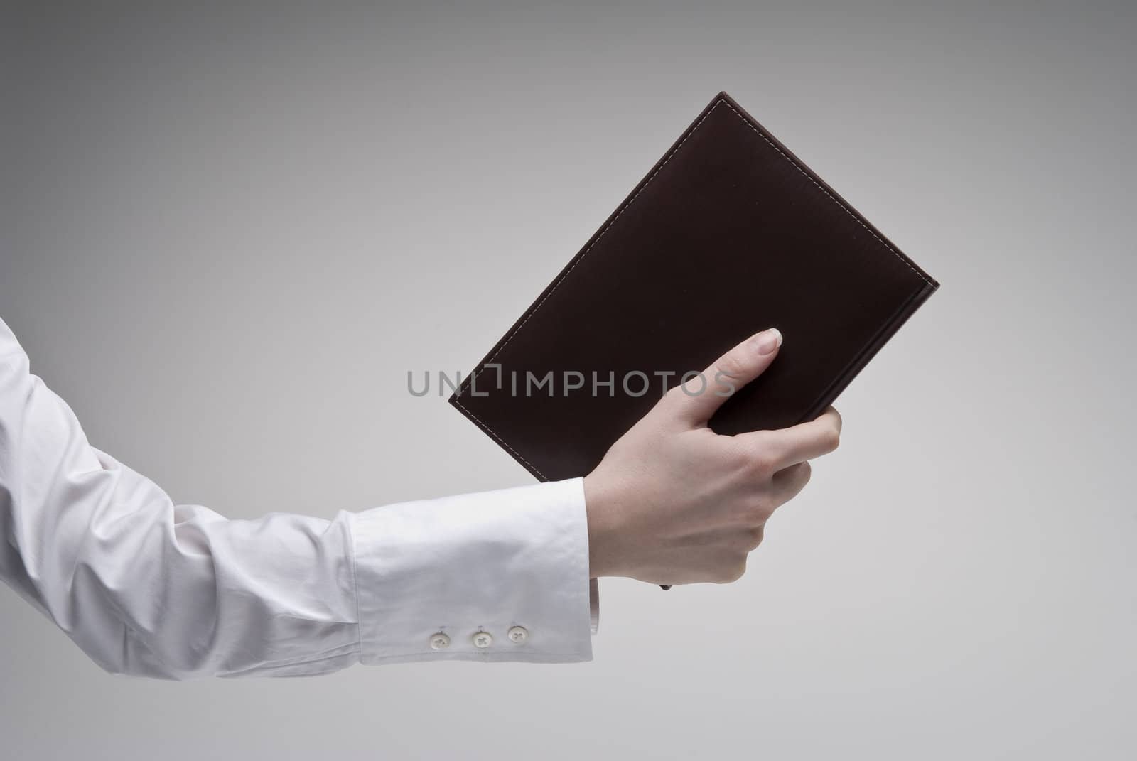 Woman's hand holding brown diary with leather hardcover over light background