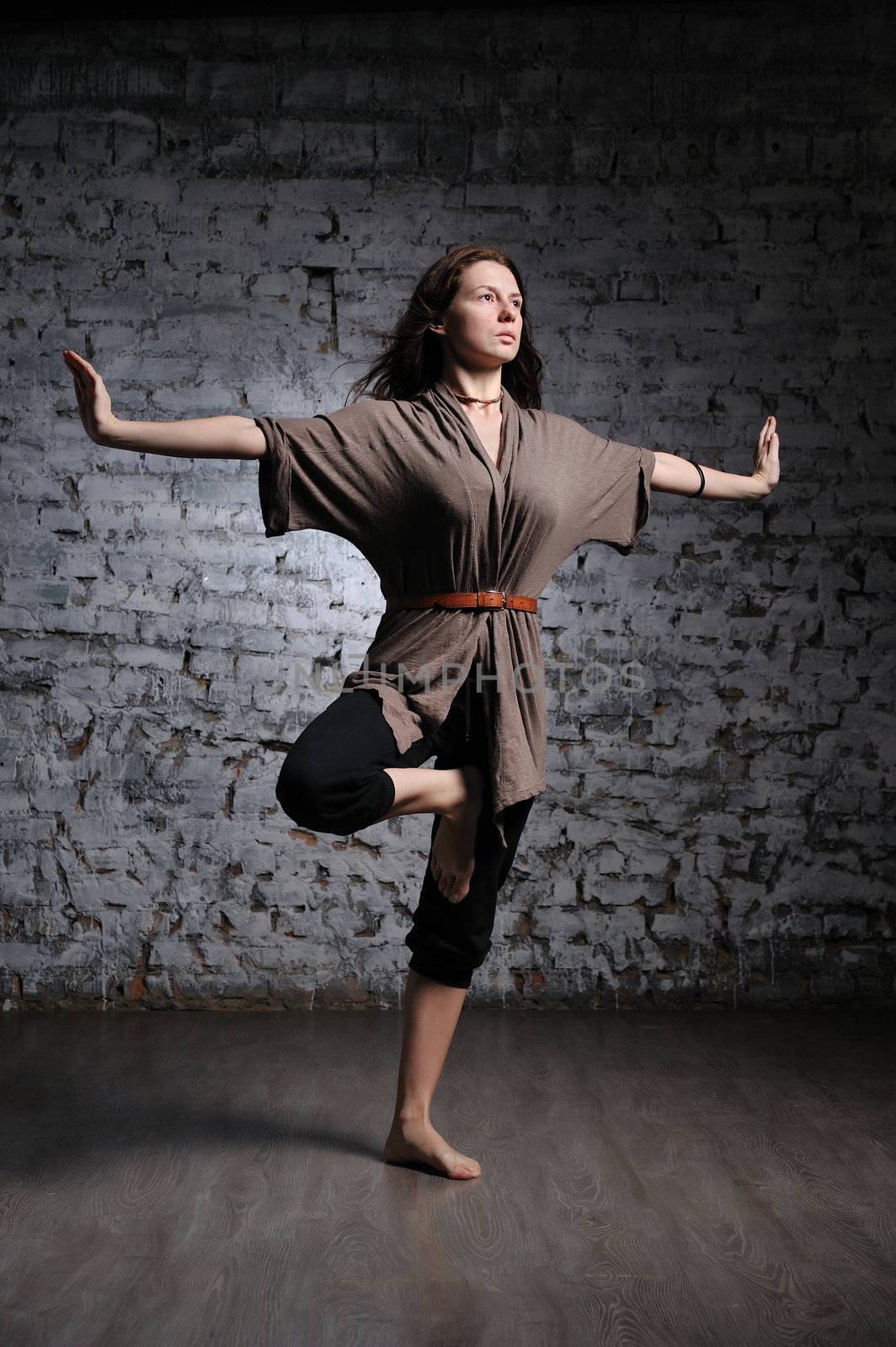 Full-length portrait of young beautiful woman doing yoga excercise against a brick wall