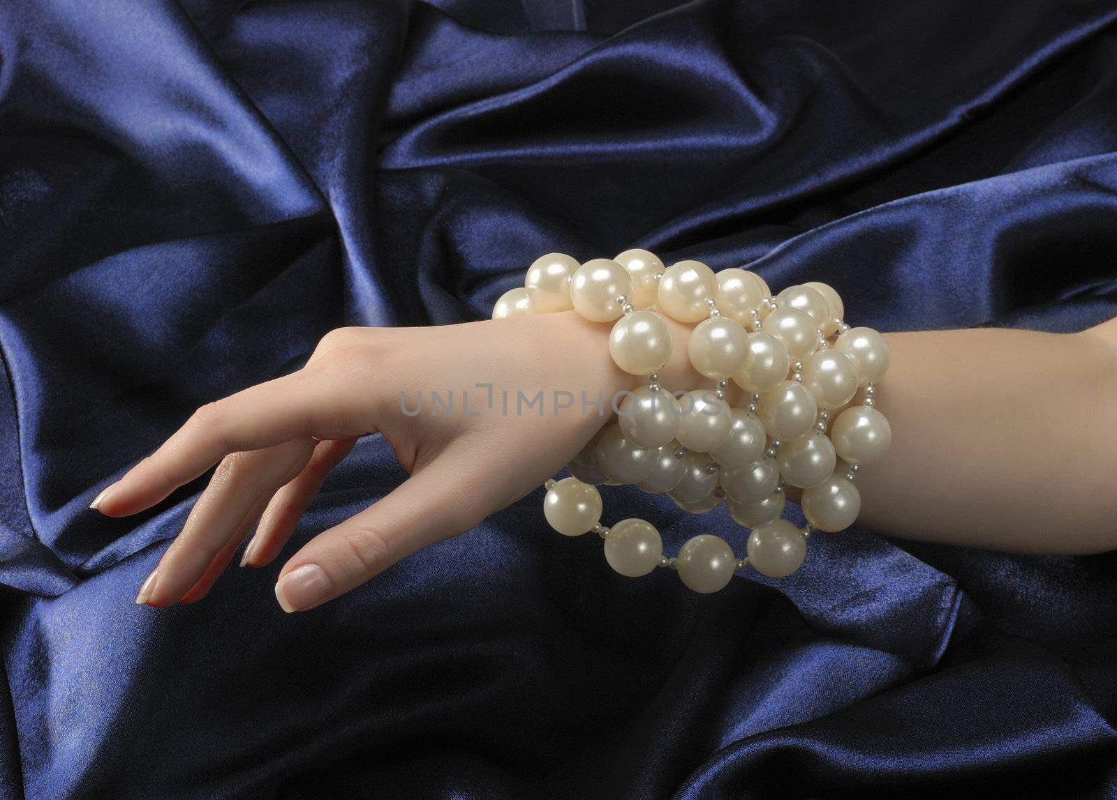 Woman's hand wearing perls necklace on blue silky background