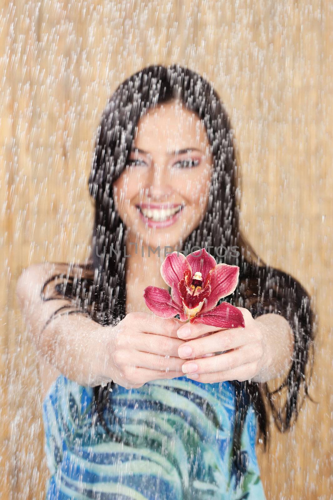 Happy girl with long hair holding red orchid under water drops in tropical environment, focus on flower