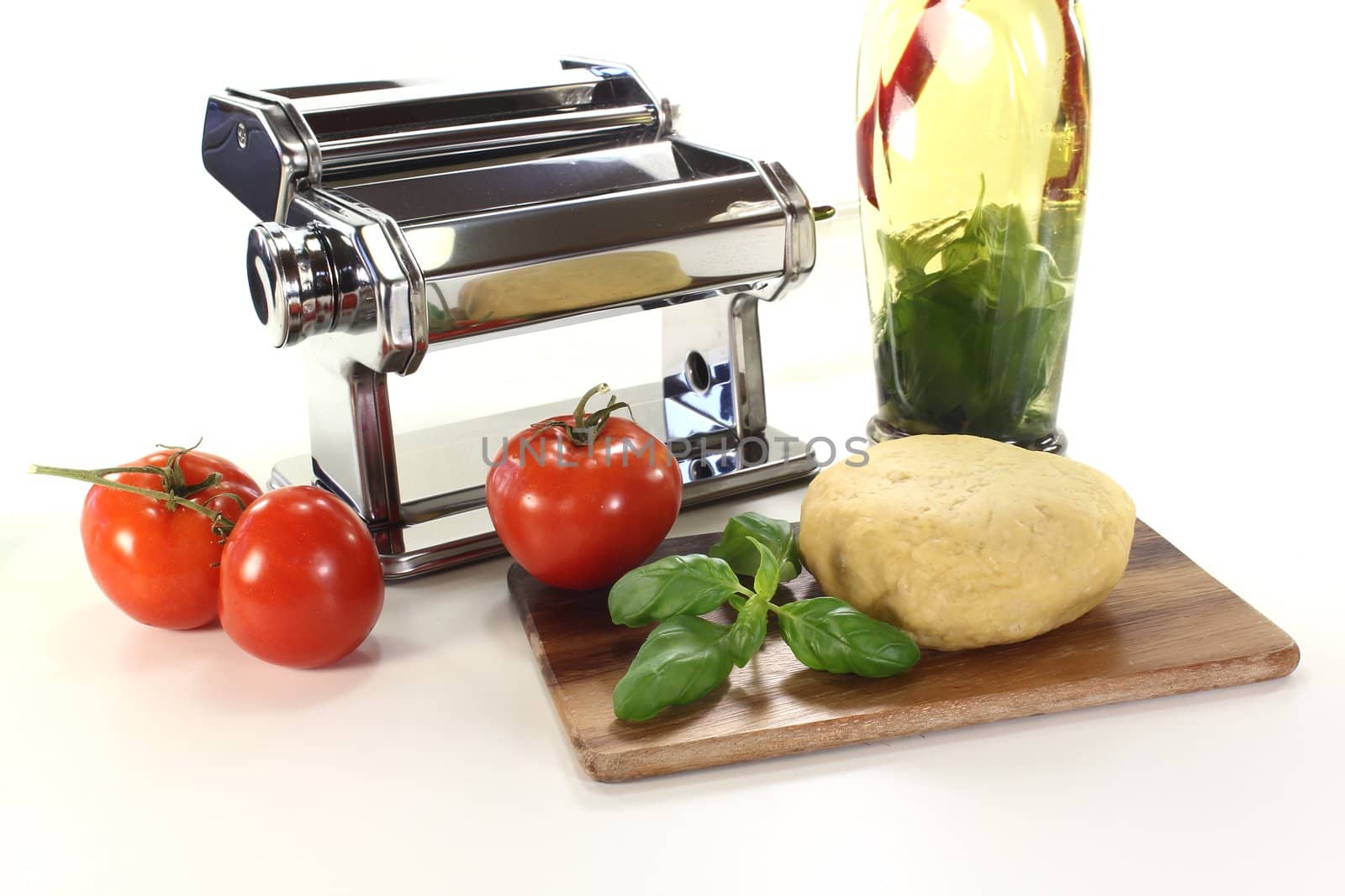 Noodle dough in a pasta machine with tomatoes, herbs oil and basil