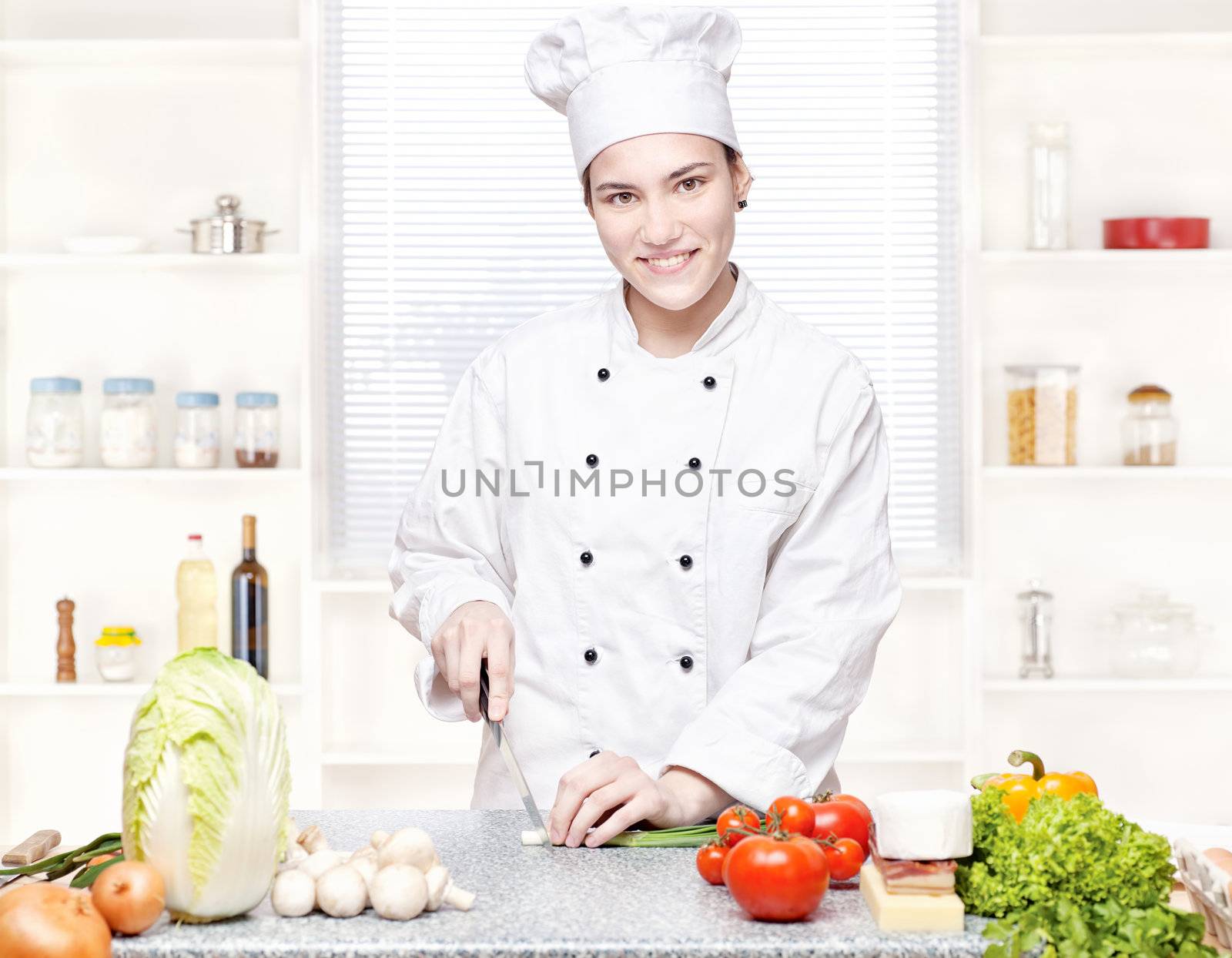 Young female chef cutting onions in kitchen