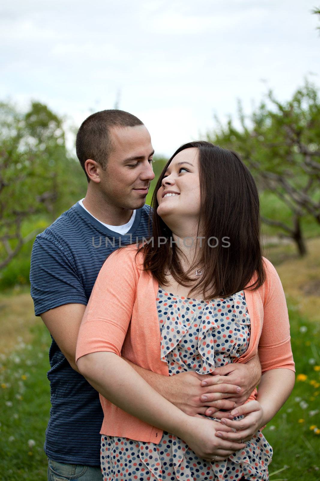 Young happy couple enjoying each others company outdoors walking through an orchard.