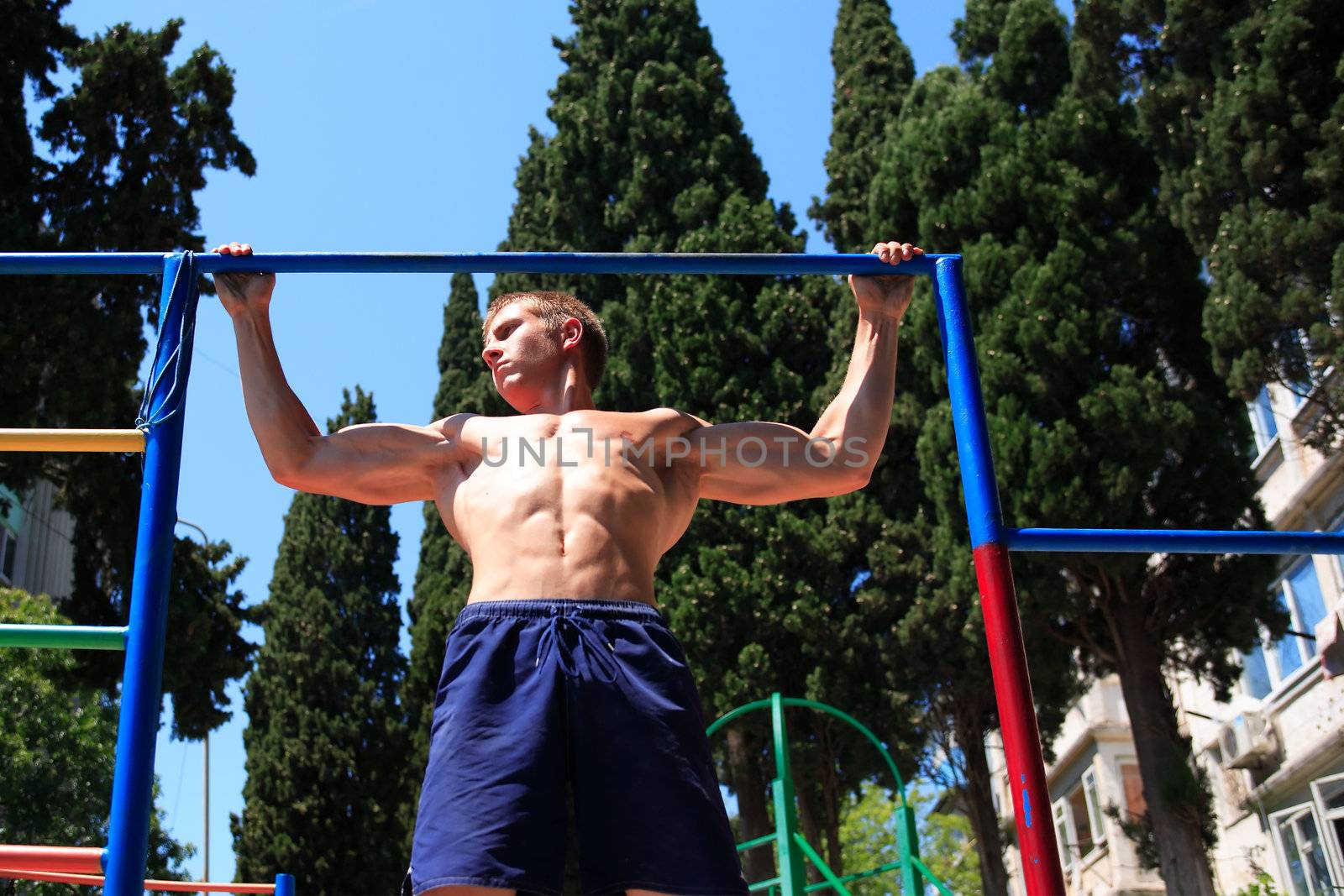 Young strong teenage athlete doing pull-up on horizontal bar
