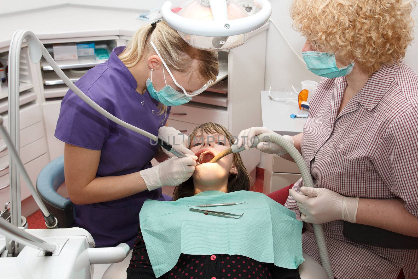 dentist with  assistant treats  a young girl teeth