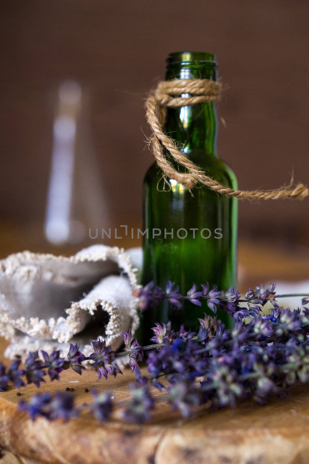 Still life composition with corded small green empty bottle, blue flowers and linen fabric. Shallow DOF