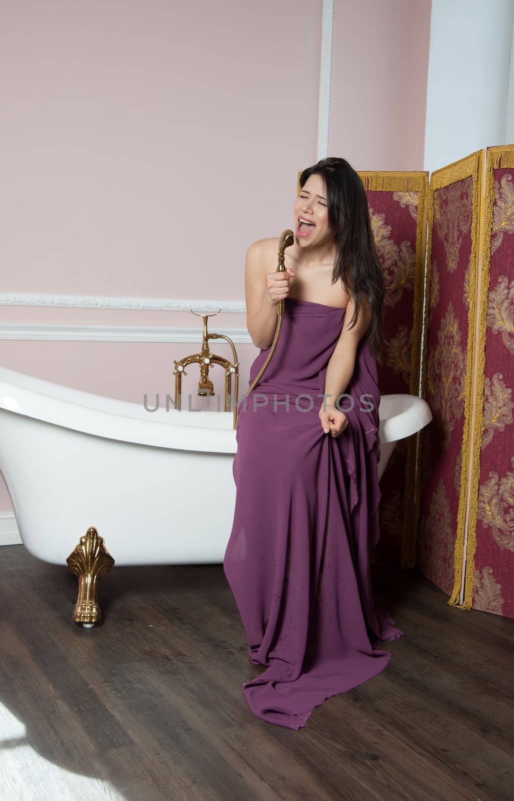 woman in tissue sings in the shower while sitting on the bathtub
