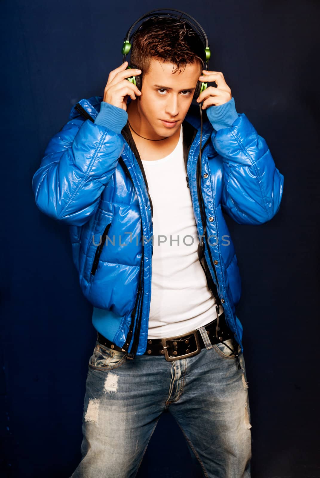 Young man listening music with headphones standing on blue ligh background