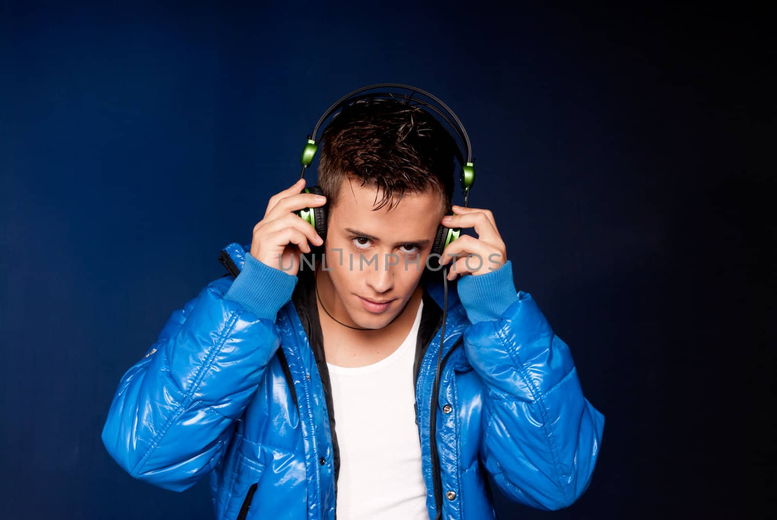 Young man listening music with headphones portrait on blue background by dgmata