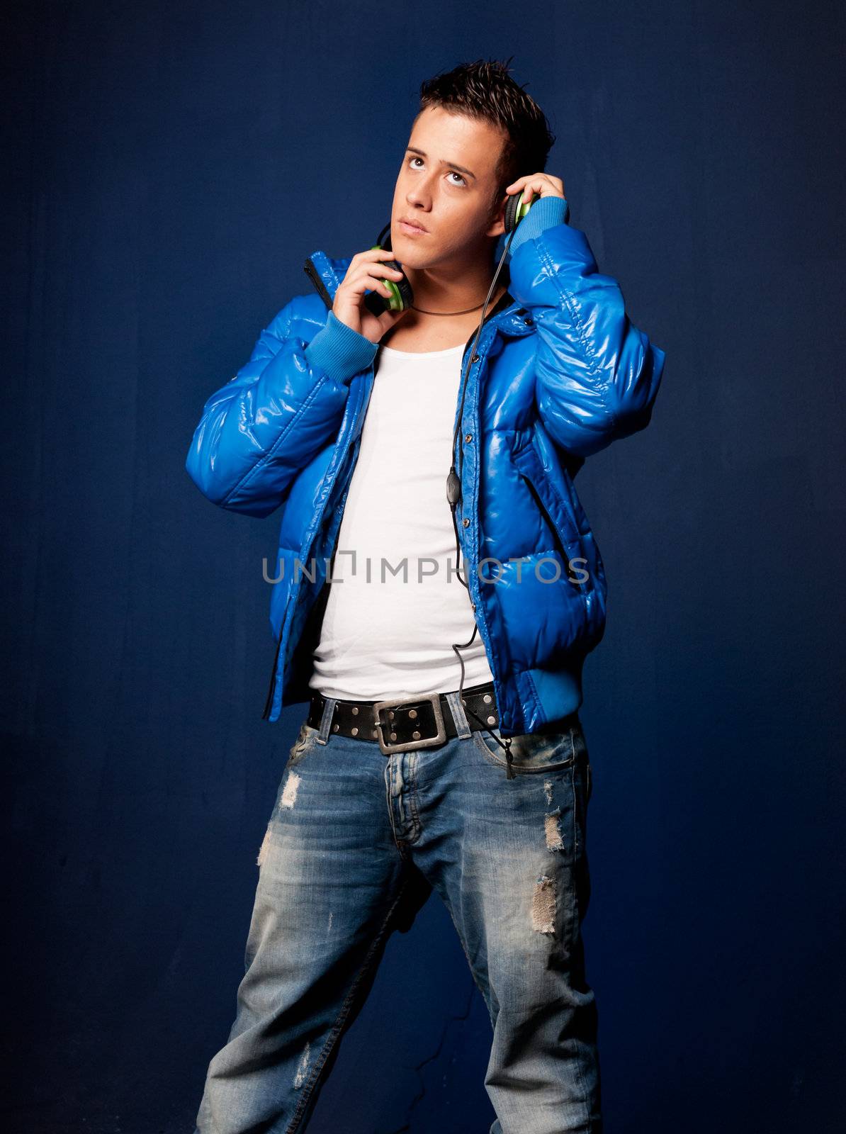Young man listening music with headphones standing on blue ligh background
