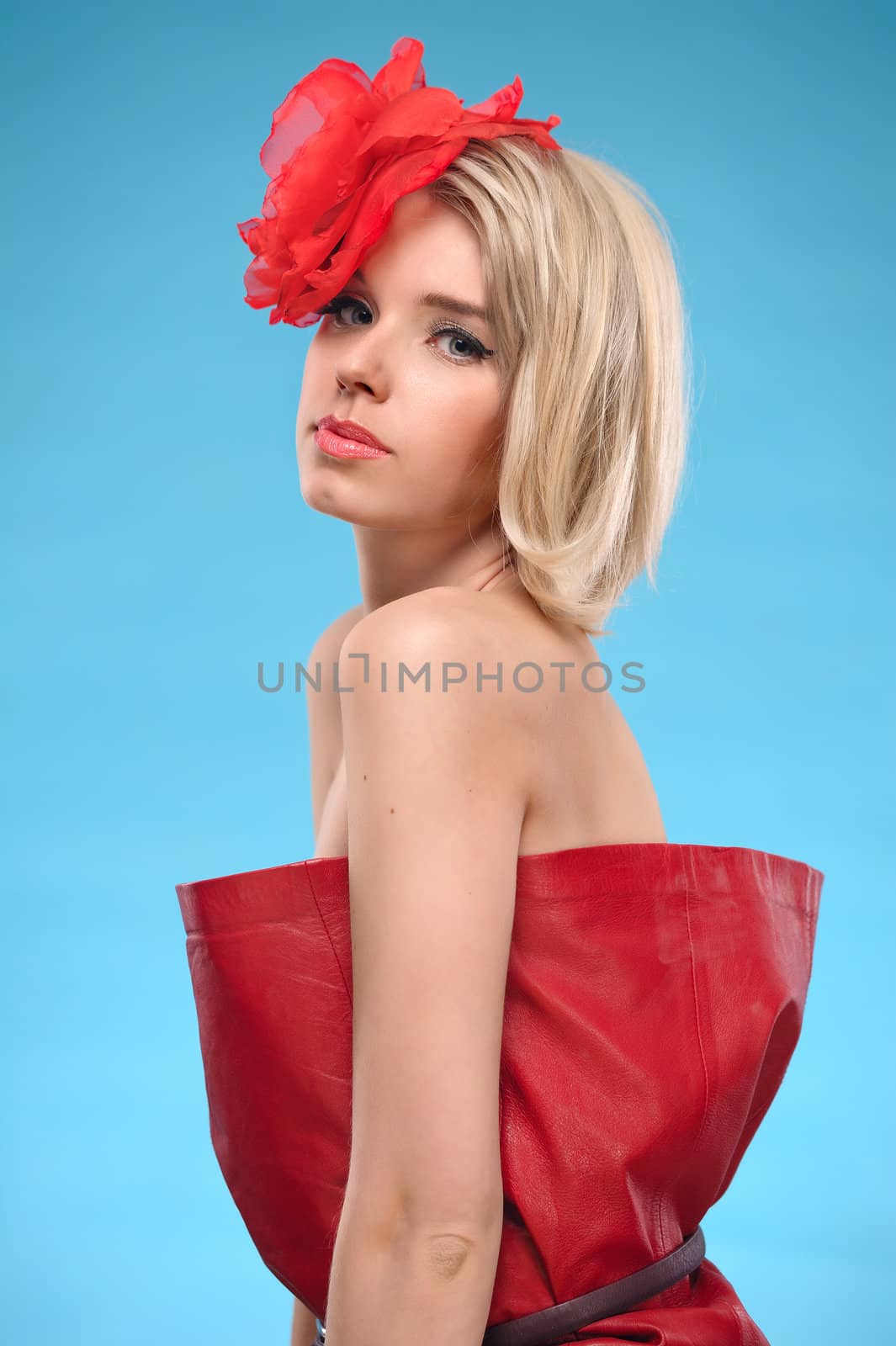 Portrait of beautiful blond woman with a red flower in her hair. Bare shoulders and fashion make-up. On a blue background