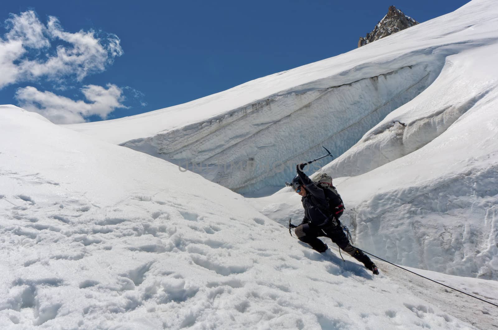 A male climber , dressed in black, climbs up a snowy slope. Winter clear sky day.