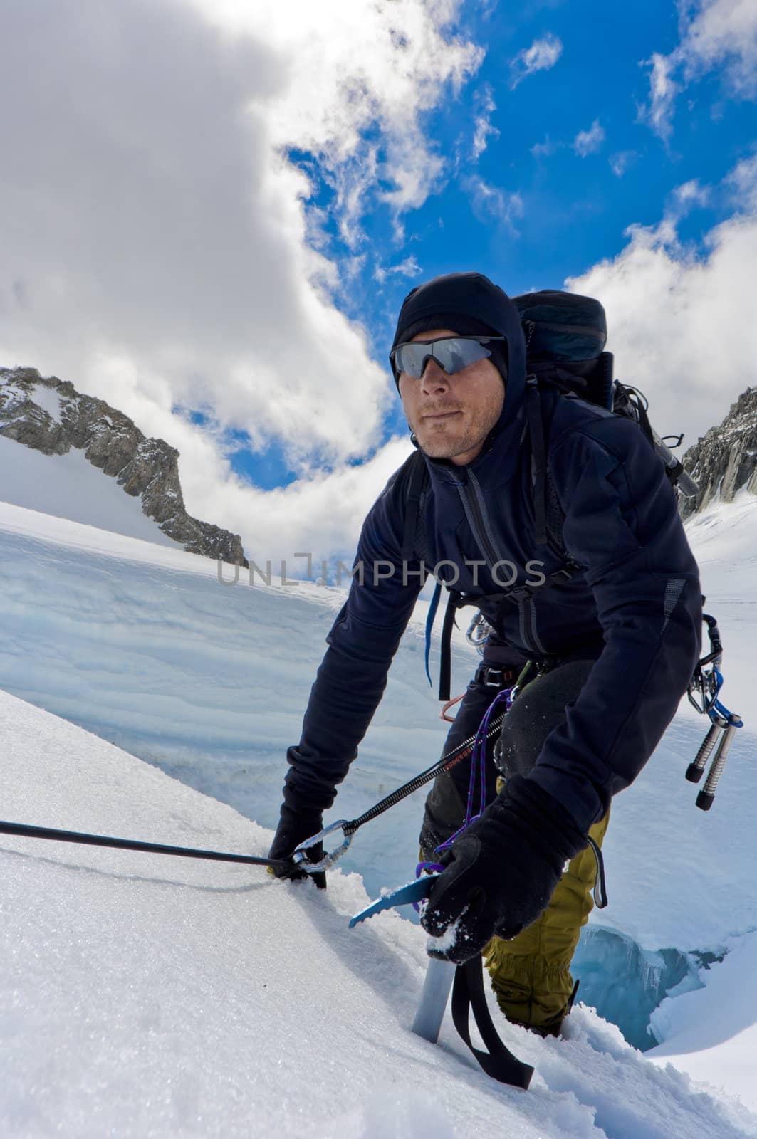 A male climber , dressed in black, climbs up a snowy slope. Winter clear sky day.