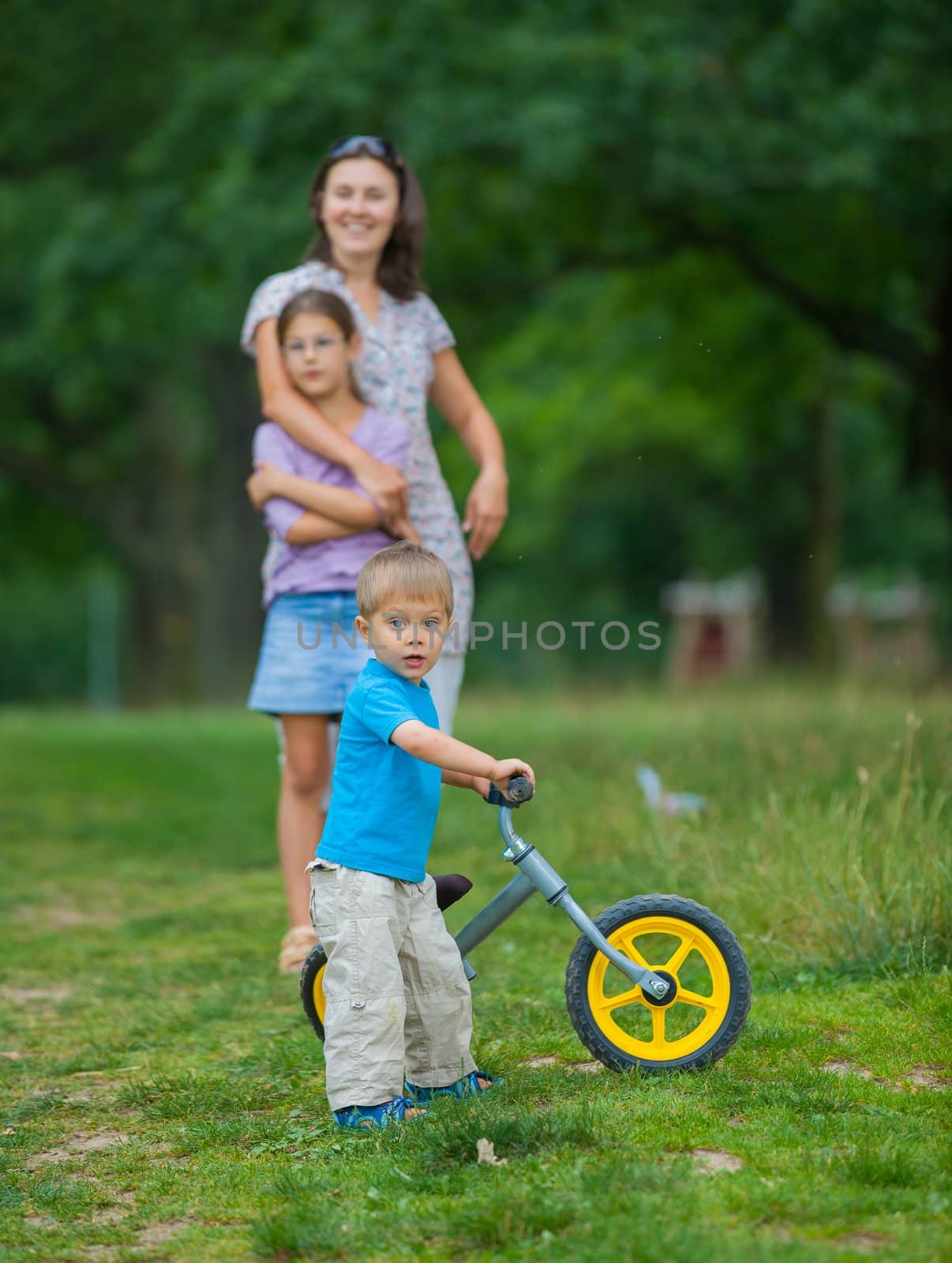 Portrait of little boy on a bicycle and his mother and sister in the summer park. Vertical view