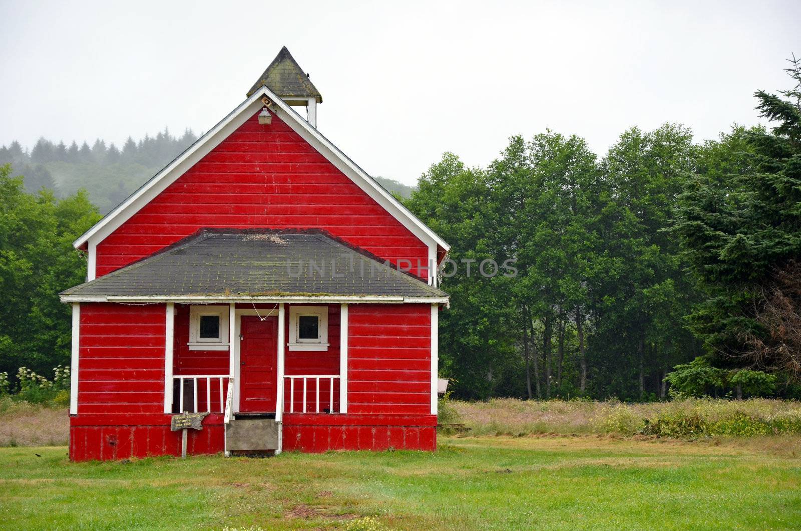 Little red schoolhouse in meadow on misty morning