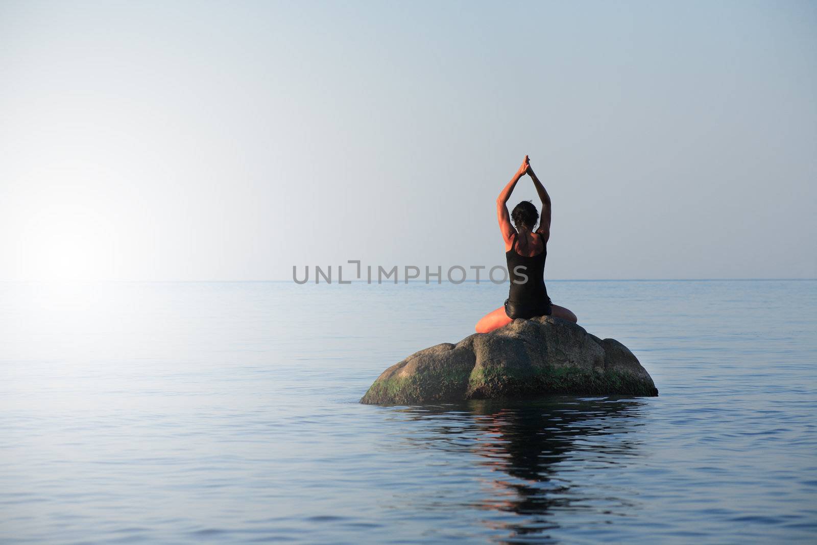 Svelte adult woman doing yoga exercise on the stone in the sea