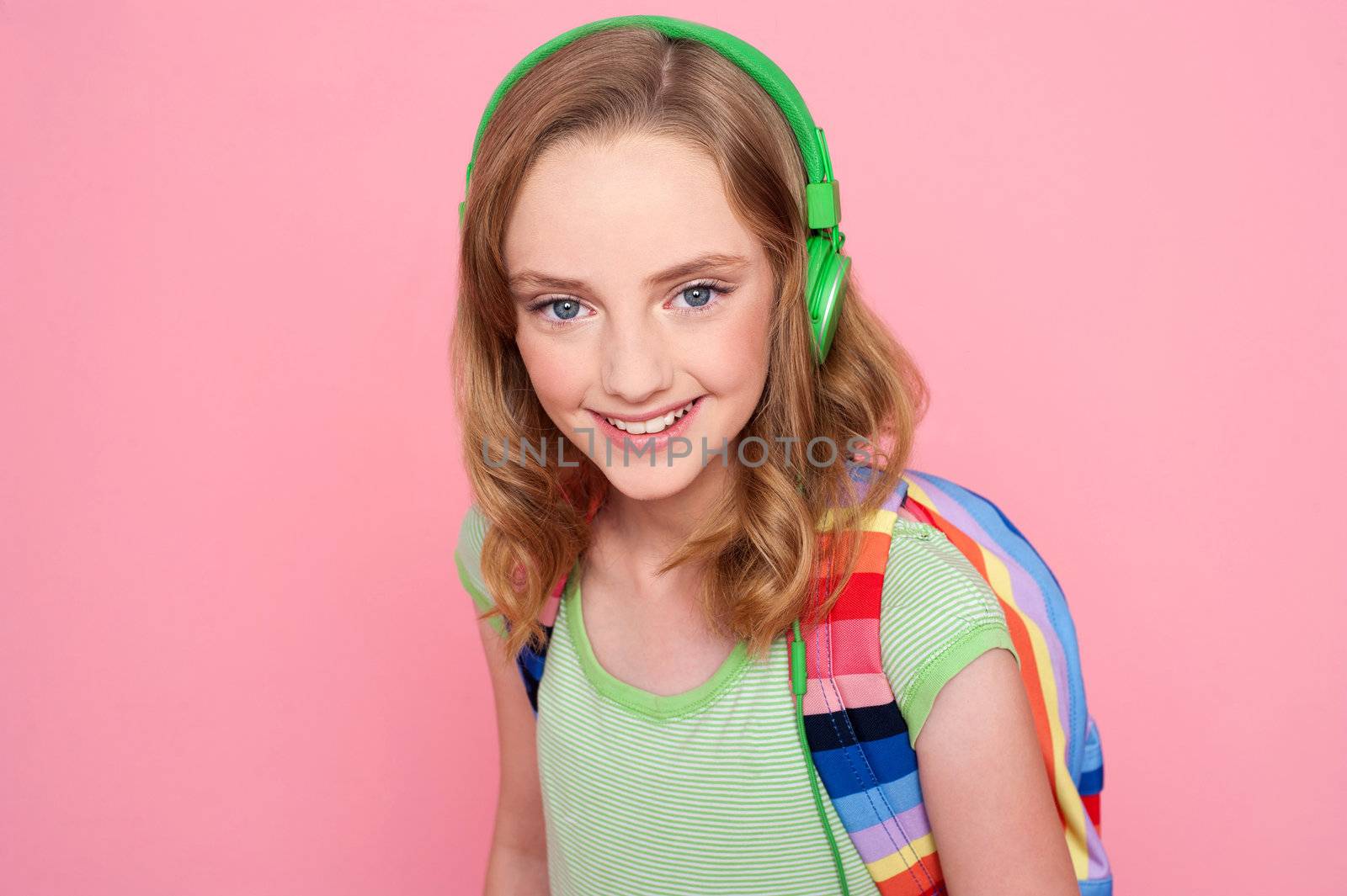 Closeup of a beautiful schoolgirl with headphone and bag isolated over pink