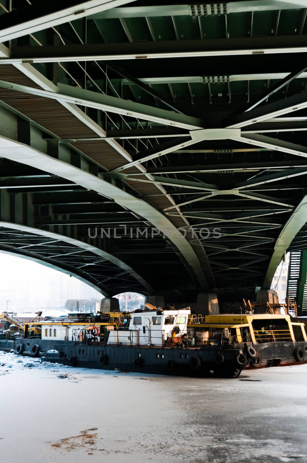 Small tugs under the green bridge at winter, channel is frozen