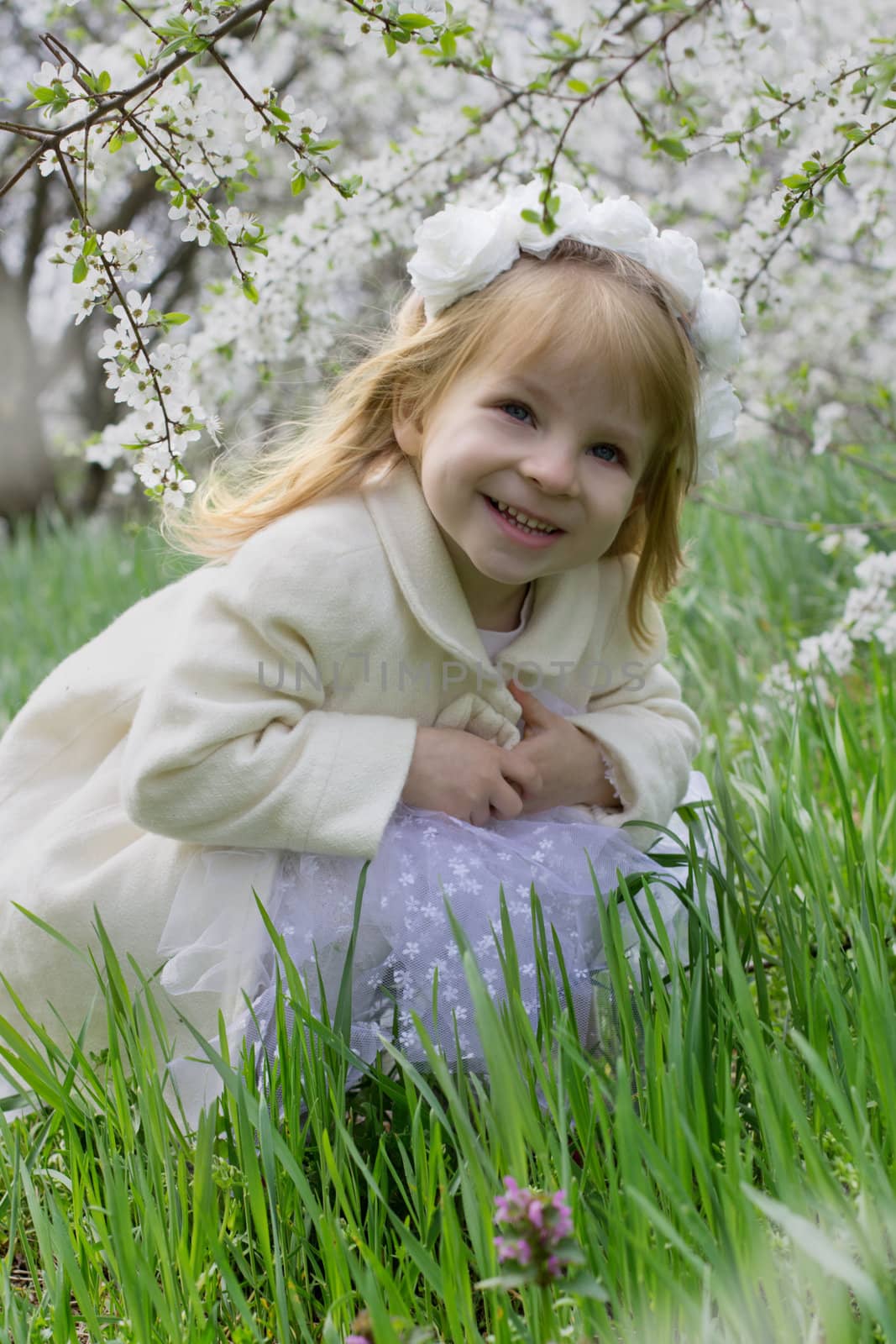 Happy smiling girl sitting among spring blossom garden
